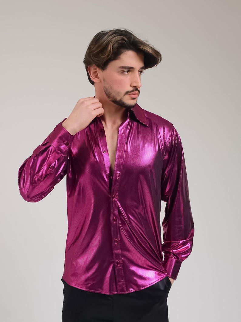 K&ouml;nnte beinhalten: Ein lang&auml;rmeliges, gekn&ouml;pftes Hemd in leuchtendem Magenta. Das Hemd hat ein gl&auml;nzendes, metallisches Finish, einen klassischen Kragen und gekn&ouml;pfte Manschetten. Das Hemd ist oben aufgekn&ouml;pft und gibt die Brust frei.