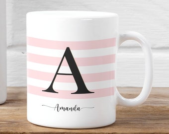 May include: White ceramic mug with pink stripes and a black letter "A" in the center. The mug has a black cursive inscription that reads "Amanda".