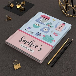 May include: A pink and blue recipe book with the text "Sophie's Recipe Book" and illustrations of kitchen tools and food.