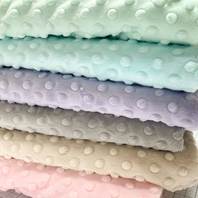 May include: Stack of five fabric squares in different pastel colors. The fabric has a textured, dotted pattern. The colors are light green, light blue, lavender, gray, and light pink.