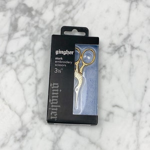 May include: A gold stork embroidery scissors in a black and blue package. The package says "gingher stork embroidery scissors 3 1/2""