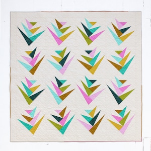 May include: A modern quilt featuring a repeating geometric pattern. The design showcases stylized, colorful shapes in teal, pink, gold, and green against a cream background. The quilt has a brown border and is likely handmade.