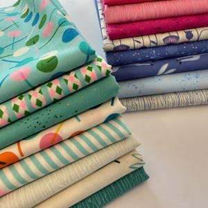 May include: A stack of fabric squares in various patterns and colors, including blue, green, pink, and white. The fabrics are arranged in a staggered pattern, with the top fabric square being a light blue with a white and green pattern.