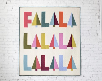 May include: A square quilt with a cream background featuring the text FA LA LA LA LA LA LA LA in colorful block letters and stylized triangular tree shapes. The design uses various shades of pink, orange, yellow, green, and blue fabric.