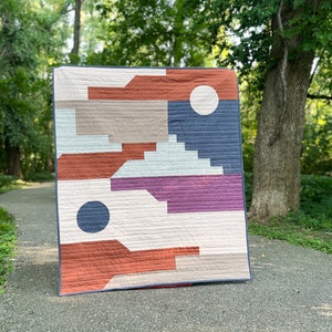 May include: A geometric quilt with a modern design. The quilt features a variety of colors, including red, orange, brown, purple, blue, and white. The quilt is made of cotton fabric and is quilted with a straight stitch.