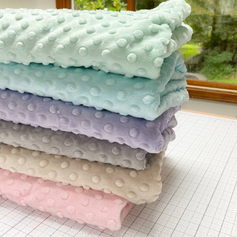 May include: A stack of five soft, plush fabrics in various pastel colors. The fabrics have a textured, dotted pattern and are folded neatly.