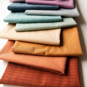 May include: A stack of 10 different colored fabric swatches. The swatches are arranged from darkest to lightest, with the darkest swatch being a dark brown and the lightest swatch being a light beige. The swatches are all made of a soft, textured fabric.