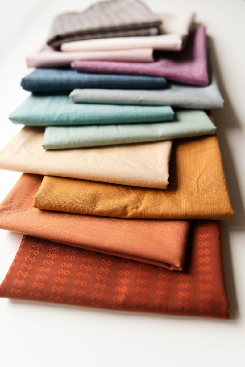 May include: A stack of 10 different colored fabric swatches. The swatches are arranged from darkest to lightest, with the darkest swatch being a dark brown and the lightest swatch being a light beige. The swatches are all made of a soft, textured fabric.