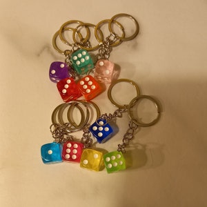 Può includere: Un set di sette portachiavi a forma di dado colorati. I dadi sono in plastica trasparente con punti bianchi. I portachiavi sono attaccati a anelli portachiavi argentati.