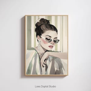 Op de afbeelding: Een aquarel schilderij van een vrouw met donker haar in een knot, die een witte zonnebril en parel oorbellen draagt. Ze draagt een gestreept shirt en heeft een neutrale uitdrukking op haar gezicht.