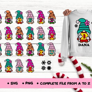 May include: A set of 26 colorful gnomes holding letters of the alphabet. Each gnome is wearing a different colored hat and has a different colored beard. The gnomes are holding the letters in front of them. The letters are in a red, yellow, and blue color scheme. The gnomes are surrounded by snowflakes. The image also shows a white sweatshirt with a gnome holding the letter D and the name Dana printed below.