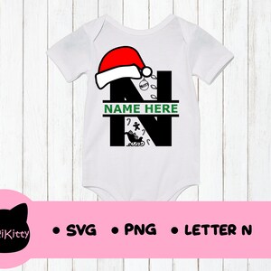 May include: White baby onesie featuring a black letter N, a red Santa hat, and green Christmas decorations. The text "NAME HERE" is written in green on a white banner.