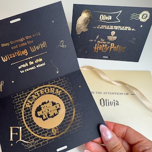 May include: Black and gold Harry Potter-themed invitation. The invitation features gold foil lettering and illustrations, including an owl and the words "Wizarding World." The invitation is designed to be scratched to reveal the date and time.