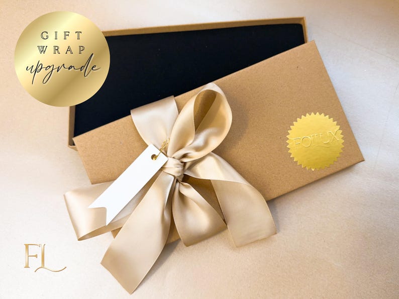 May include: A gift box with a black interior, wrapped with a cream-colored satin ribbon and a blank tag. The box is brown with a gold foil sticker. The words "GIFT WRAP upgrade" are in a gold circle.