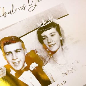 May include: A black and white photograph of a couple, likely a wedding photo, with gold foil accents. The text "50 Fabulous Years" is written in gold script. The woman wears a crown and veil.