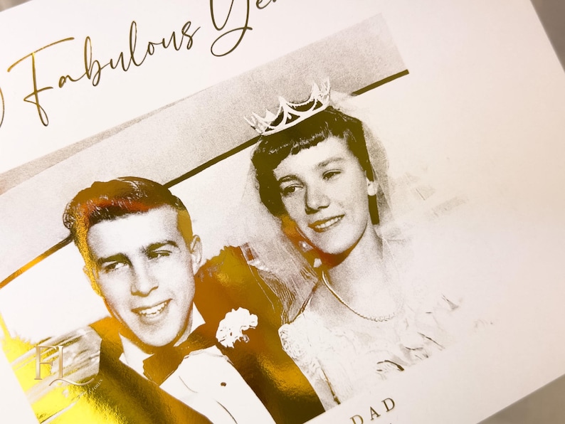 May include: A black and white photograph of a couple, likely a wedding photo, with gold foil accents. The text "50 Fabulous Years" is written in gold script. The woman wears a crown and veil.