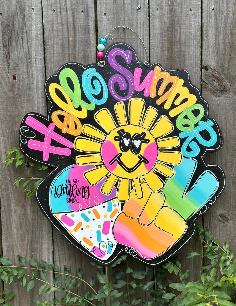 May include: A colorful wooden sign with the words "Hello Summer" in various bright colors. The sign features a smiling sun, a peace sign, and a section with sprinkles. The sign is designed to hang and has a wire and beaded accent.