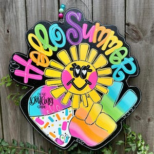 May include: A wooden sign with the words "Hello Summer" in colorful lettering. The sign features a smiling sun, a peace sign, and a section with sprinkles. The sign is black with a white border and a wire hanger.