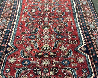 May include: A red, blue, and cream colored rug with a geometric pattern. The rug has a border with a repeating pattern of diamonds and triangles.