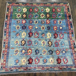 Könnte beinhalten: Rechteckiger Teppich mit geometrischem Muster. Der Teppich hat einen grünen oberen Bereich, einen blauen Mittelteil und einen blau-grünen unteren Bereich. Das Design umfasst sich wiederholende paisleyartige Formen in verschiedenen Farben, darunter Rot, Blau und Gelb.