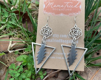 May include: Silver-toned earrings featuring a rose design at the top, a lightning bolt within a triangle, and a hook closure. The earrings are displayed on a brown card with the text "MamaTried NoogaDyed".