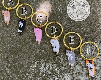 Può includere: Sei portachiavi dorati con ciondoli di gatto di diversi colori. Ogni portachiavi ha una lettera da A a F sull'anello. I ciondoli sono neri, rosa, bianchi, grigi e arancioni e bianchi.