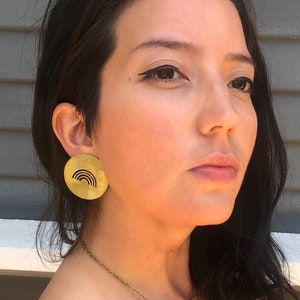 May include: A woman wearing a pair of gold earrings with a rainbow cutout design.