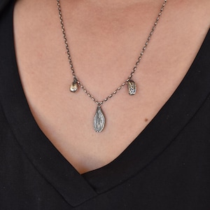 May include: A silver necklace with three charms. The charms are a teardrop shape, a small round shape, and a larger oval shape. The necklace is on a model wearing a black shirt.