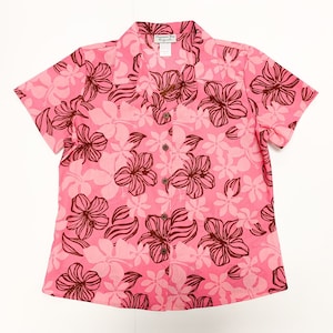 May include: A pink short-sleeved button-down shirt with a brown floral print. The shirt has a collar and a button closure.
