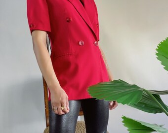 Puede incluir: Una chaqueta roja de manga corta con cierre de doble botonadura y dos botones grandes. La chaqueta tiene un bolsillo único en el lado izquierdo.