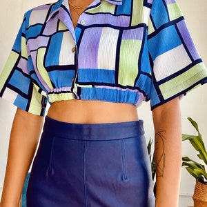 Puede incluir: Una camisa de botones de corte corto con estampado geom&eacute;trico azul, morado y verde, con cintura el&aacute;stica fruncida.
