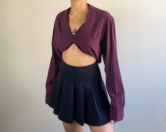 Puede incluir: Una camisa de manga larga de color burdeos con un nudo en la parte delantera y una falda plisada negra.