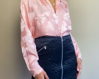 Puede incluir: Una blusa de satén rosa con estampado floral y una falda negra acolchada con cremallera en la parte delantera.