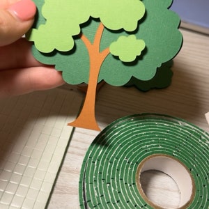 May include: A green paper craft tree with a brown trunk and a roll of green double-sided tape.