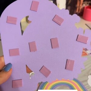 May include: Purple foam tape squares on a purple cardstock background. The cardstock is cut into the shape of a cloud. The text "BUY FOAMIES HERE" and "Purple Foam Tape" are visible in the image.