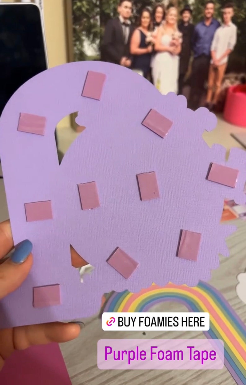 May include: Purple foam tape squares on a purple cardstock background. The cardstock is cut into the shape of a cloud. The text "BUY FOAMIES HERE" and "Purple Foam Tape" are visible in the image.