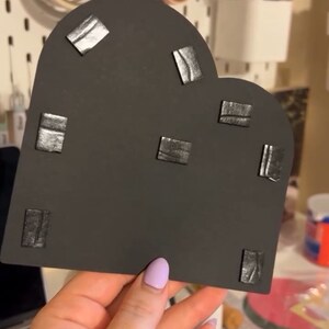 May include: A black heart-shaped piece of foam with multiple small black adhesive squares attached to the surface.