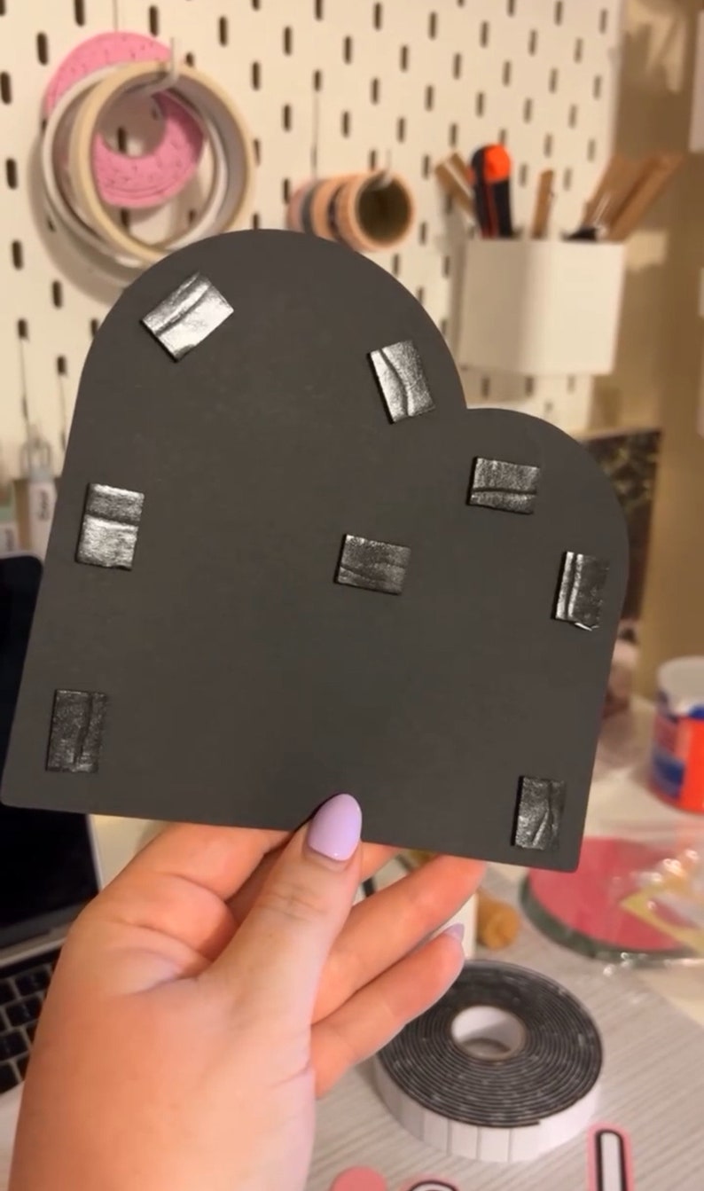 May include: A black heart-shaped piece of foam with multiple small black adhesive squares attached to the surface.