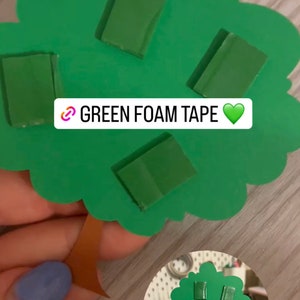 May include: Green foam tape pieces are attached to a green paper tree cutout. The text "GREEN FOAM TAPE" is written on the tree.