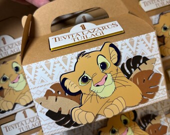 Op de afbeelding: Bruine kartonnen party-favour boxen met een leeuwenfiguur uit de film The Lion King. De dozen hebben een gouden rand en de tekst "1 TEVITA LAZARUS TUILAGI" gedrukt op de voorkant.
