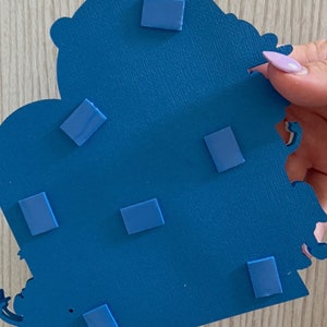 May include: Blue cardboard cutout of a castle with a crown on top. The back of the cutout has several adhesive squares attached to it.