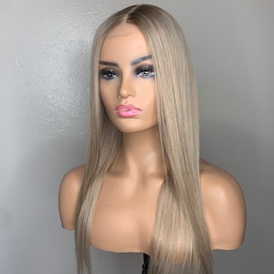 Może przedstawiać: Długa, prosta, jasnoblond peruka z naturalnym przedziałkiem. Peruka jest ułożona w gładki, prosty styl i sięga do ramion.