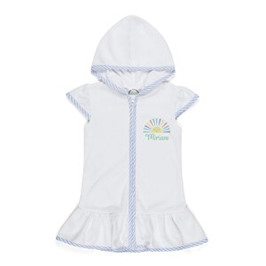 Peut inclure: Robe de plage blanche &agrave; capuche avec fermeture &eacute;clair et ourlet &agrave; volants. La robe pr&eacute;sente un motif de soleil color&eacute; et le nom "Miriam" en &eacute;criture cursive. Les bords sont bord&eacute;s d'un motif ray&eacute; bleu et blanc.