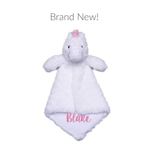 Puede incluir: Una manta de seguridad de peluche de unicornio blanco con tela suave y texturizada. La cabeza del unicornio tiene un peque&ntilde;o cuerno rosa y ojos oscuros. La manta est&aacute; bordada con el nombre Blake en rosa. Sobre el juguete, el texto dice Brand New!