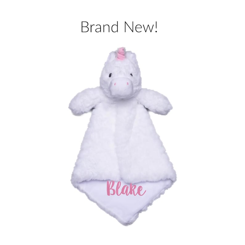Puede incluir: Una manta de seguridad de peluche de unicornio blanco con tela suave y texturizada. La cabeza del unicornio tiene un peque&ntilde;o cuerno rosa y ojos oscuros. La manta est&aacute; bordada con el nombre Blake en rosa. Sobre el juguete, el texto dice Brand New!