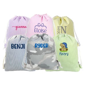 May include: A collection of drawstring bags in various colors and patterns. Each bag features a name embroidered in a contrasting color. The bags include names like "Gianna", "Eloise", "Benji", "Ryder", "Henry", and "EN".