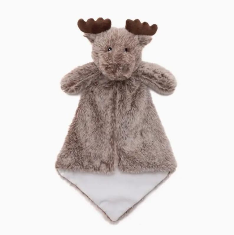 Puede incluir: Una manta de seguridad de peluche con forma de alce, con un cuerpo de piel sint&eacute;tica peluda de color marr&oacute;n claro, astas de color marr&oacute;n oscuro y una parte inferior de tela blanca lisa y s&oacute;lida. La cabeza est&aacute; unida a una base.