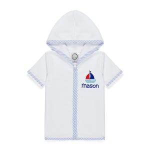 Peut inclure: Peignoir blanc &agrave; capuche et manches courtes, bord&eacute; de rayures bleues et blanches. Motif de bateau &agrave; voile rouge, bleu et blanc, avec le nom "Mason" brod&eacute; en bleu marine. Fermeture &eacute;clair int&eacute;grale.