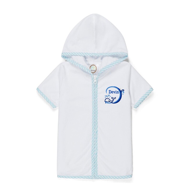 Peut inclure: Peignoir de plage blanc &agrave; capuche avec une bordure ray&eacute;e bleue et blanche. Le peignoir a une fermeture &eacute;clair et des manches courtes. Un cercle bleu avec le nom "Devin" et un motif de baleine est sur le devant.
