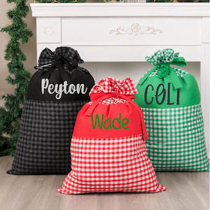 May include: Three fabric gift sacks with drawstring closures. The left sack is black and grey buffalo check with the name Peyton in white. The center sack is red and white gingham with the name Wade in green. The right sack is green and white gingham with the name Colt in black.